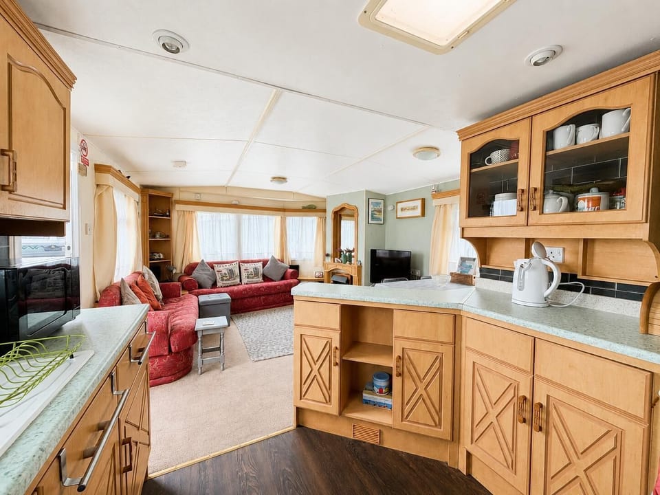 Light wood cabinetry lines the kitchen, flowing into a living area with red patterned sofas and cream curtains.