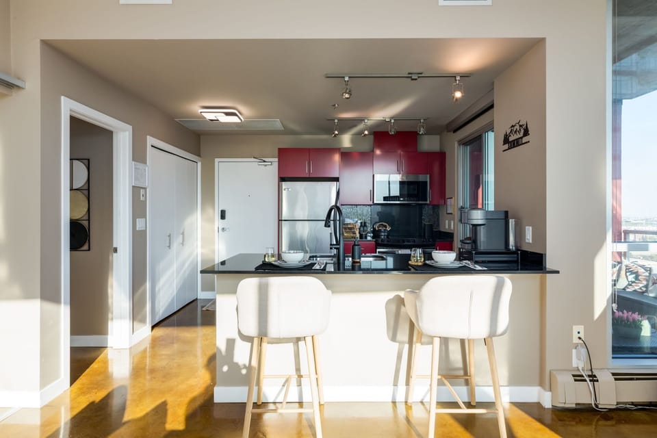 Bright and modern kitchen with bold red cabinets, black countertops, and stainless steel appliances. A cozy breakfast bar with seating for two creates the perfect space for dining or entertaining in this stylish, open-concept condo.
