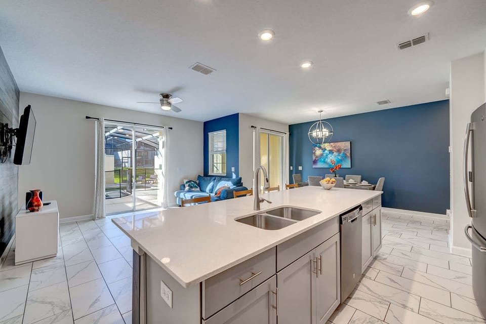 Modern kitchen island with seating opens to a bright living and dining area with blue accent walls.