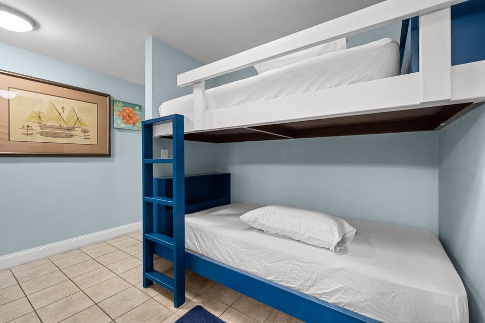 Compact room featuring a blue bunk bed with clean white linens and soft blue walls.