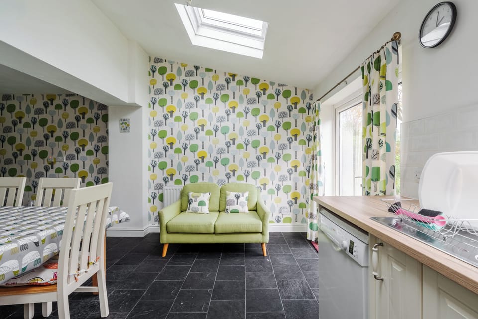 A bright, spacious kitchen with ample counter space, cabinet lighting, dishwasher, etc, and all essentials. Features a six-seater dining table, two-seater sofa, and double doors opening to the large garden—perfect for cooking, dining, and relaxing.