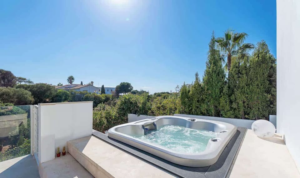 A bubbling hot tub on a sunny terrace, framed by glass rails and lush greenery, invites relaxation.