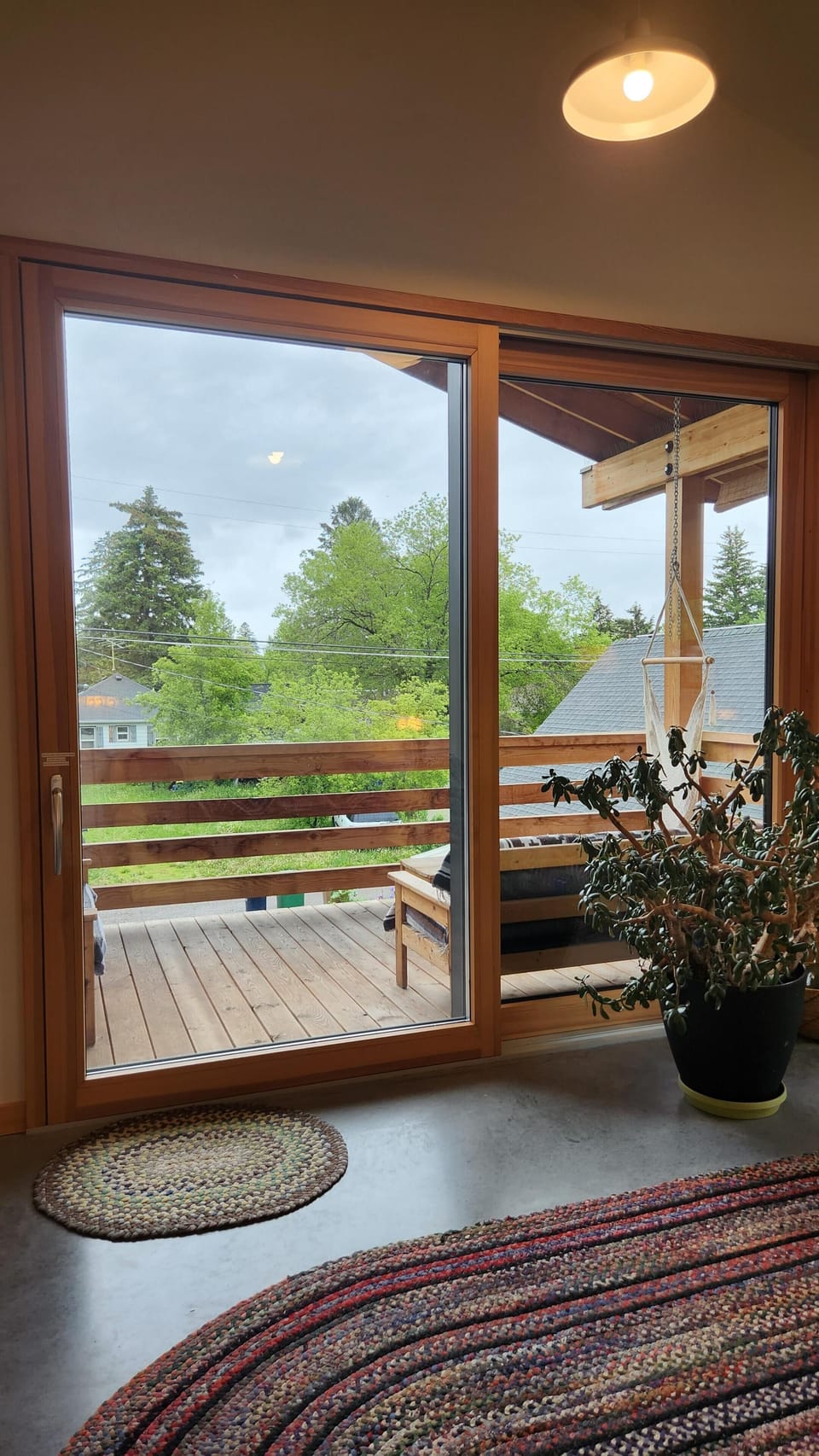 Sliding glass door opens to a wood-plank balcony with railing, outdoor bench, and leafy green views.