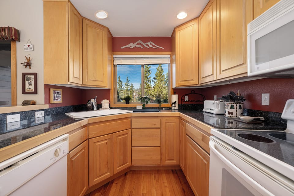 Step into your fully equipped mountain kitchen featuring warm wood cabinets, granite counters, and scenic forest views perfect for cooking memorable meals.