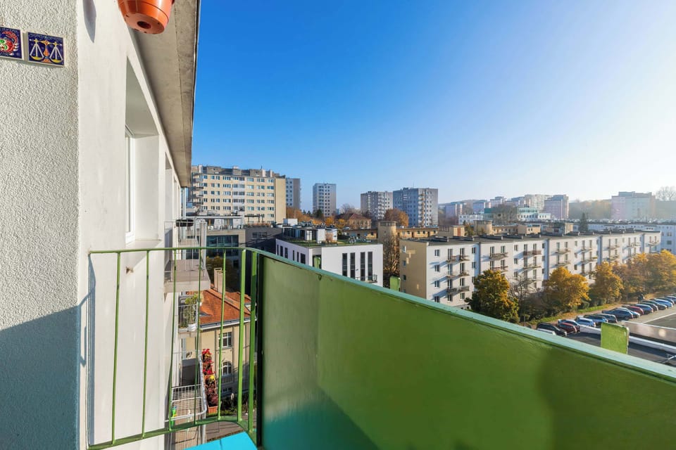 A balcony view overlooking nearby residential buildings and rooftops. The sunny weather enhances the urban view.