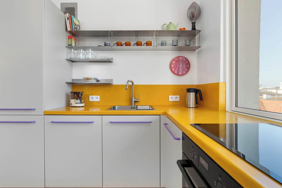 Another angle of the yellow-accented kitchen, featuring open shelves and a window view. The layout maximizes space.