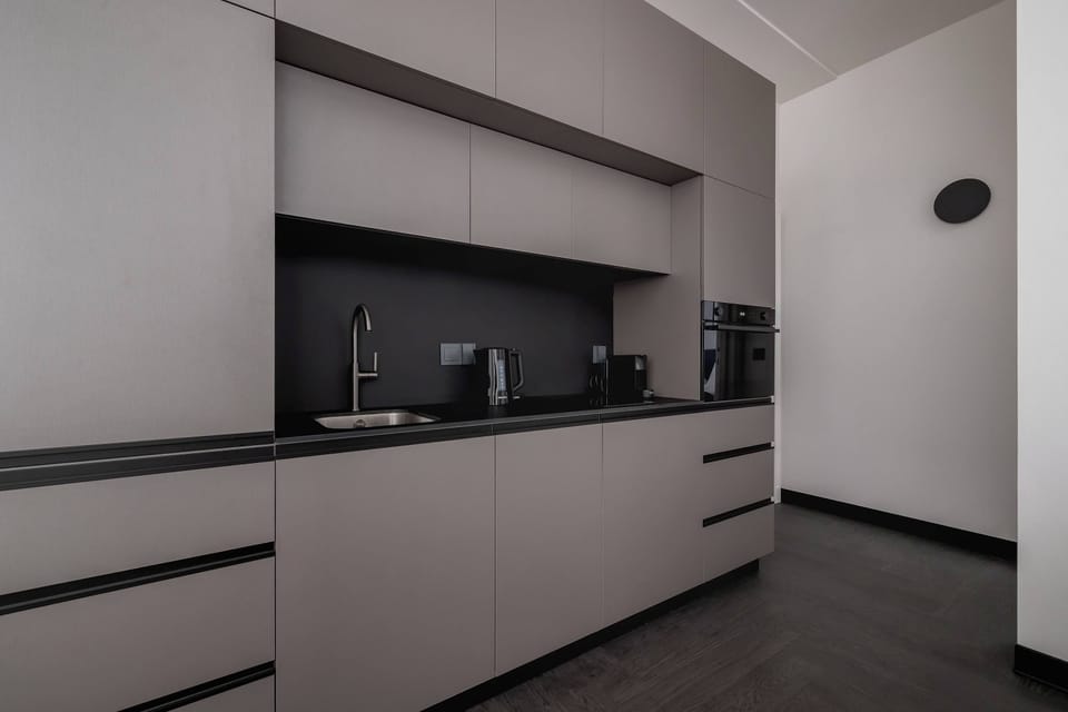A stylish kitchen with dark countertops, beige cabinetry, and modern lighting fixtures.