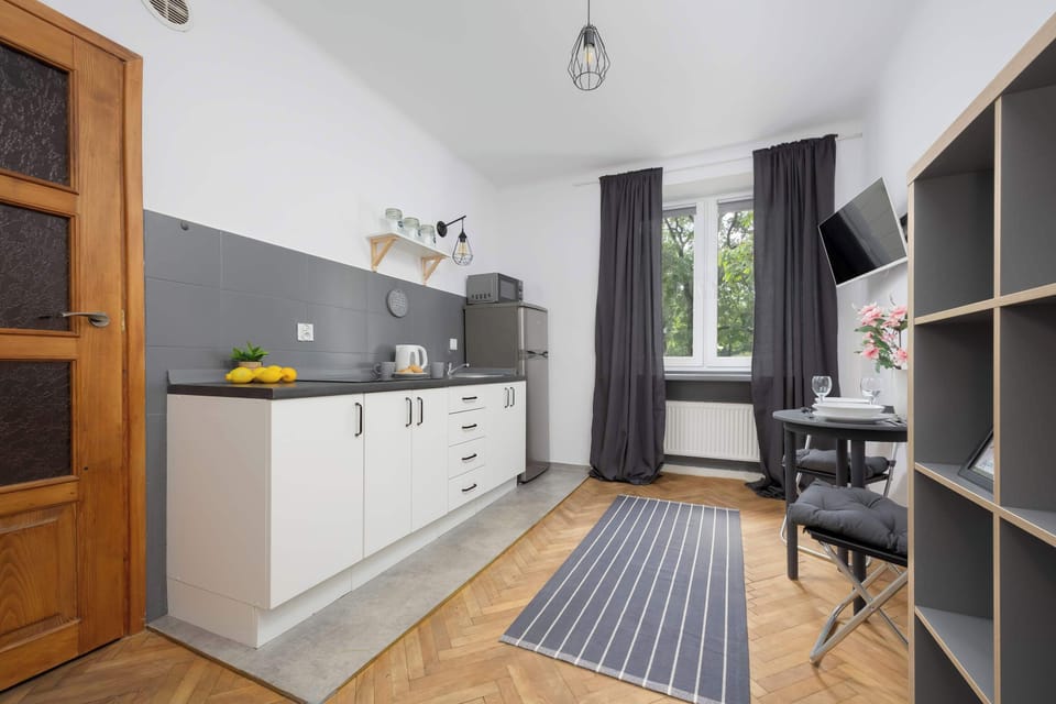 The kitchenette along one wall, featuring white cabinets, a gray countertop, and basic appliances. The wooden door and parquet flooring add warmth to the space.