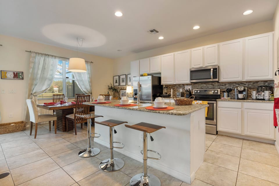 This bright kitchen boasts sleek white cabinetry and a spacious island perfect for casual dining. Natural light fills the space, accentuating the stylish bar stools and warm tile flooring for an inviting cooking atmosphere.