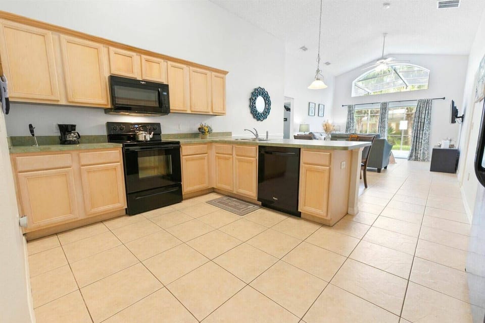 This bright, spacious kitchen with light wood cabinetry and sleek black appliances offers a functional atmosphere. High ceilings and large windows bring in natural light and stunning outdoor views, enhancing the inviting feel.