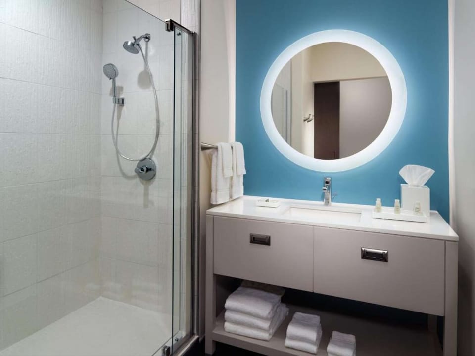 Bathroom with blue wall, round mirror, and glass shower door