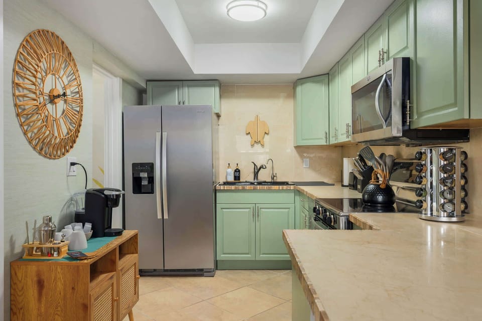 Fully equipped kitchen with soft green cabinetry, stainless appliances, and spacious counters. Enjoy cooking with ease, morning coffee at the prep station, and a bright, beachy feel that makes meals a pleasure.