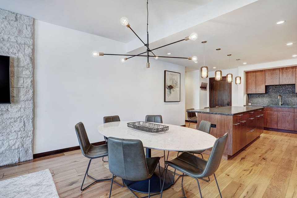 Modern dining table with seating for six, accented by a striking chandelier and stone accent wall.