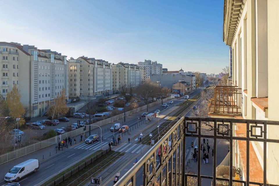 A city balcony with a black railing overlooking residential buildings. The view is open and urban.