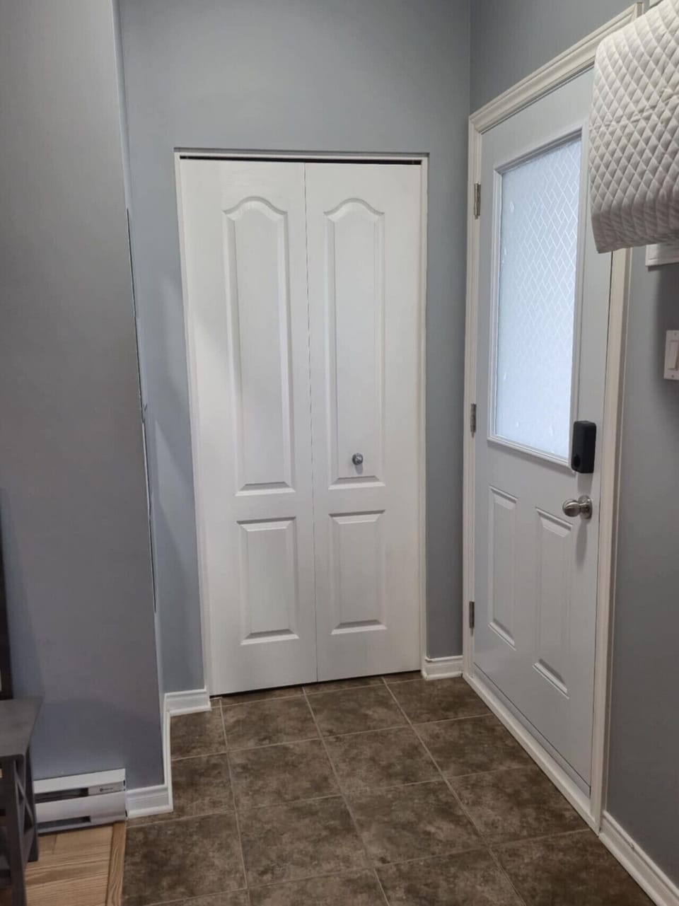 Bright, clean entryway featuring a modern frosted-glass door, fresh gray walls, and a spacious double closet—perfect for convenient, organized arrivals. Ideal first impression for your stay!
