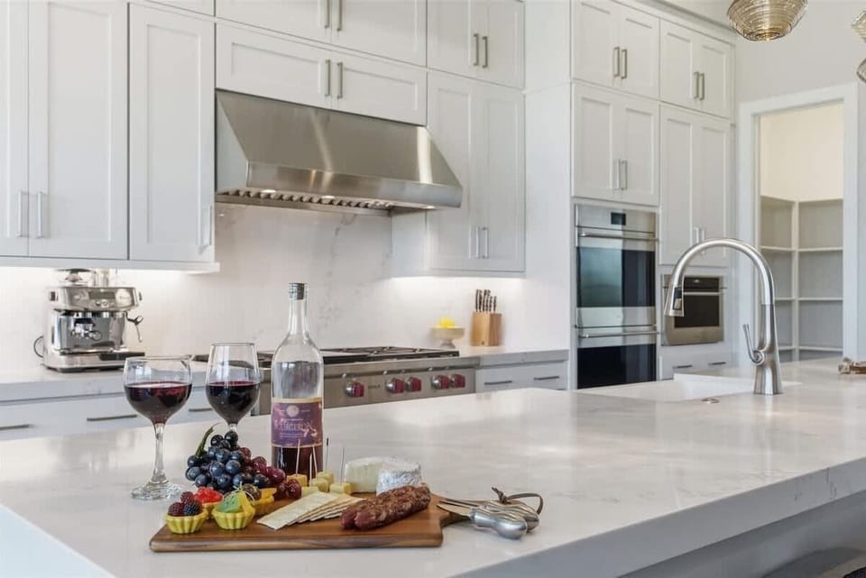 Full Kitchen features sleek white cabinetry, a spacious waterfall island with seating, and modern stainless steel appliances perfect for cooking and gathering.