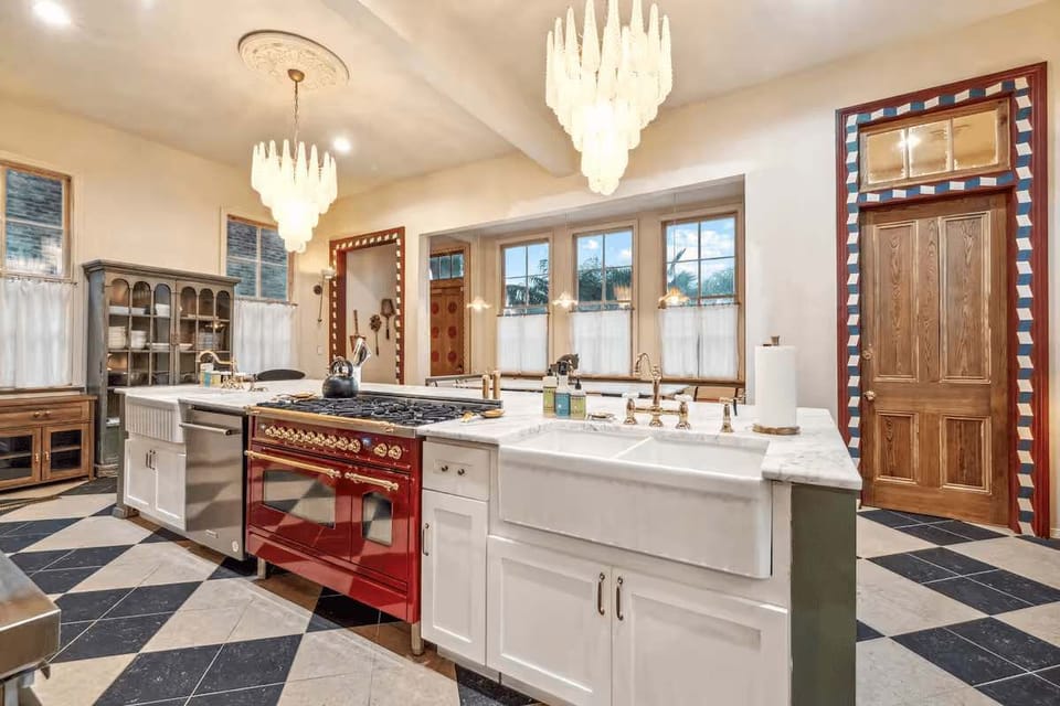 Chef’s kitchen with a large center island, farmhouse sinks, a high-end red range, and statement chandeliers.