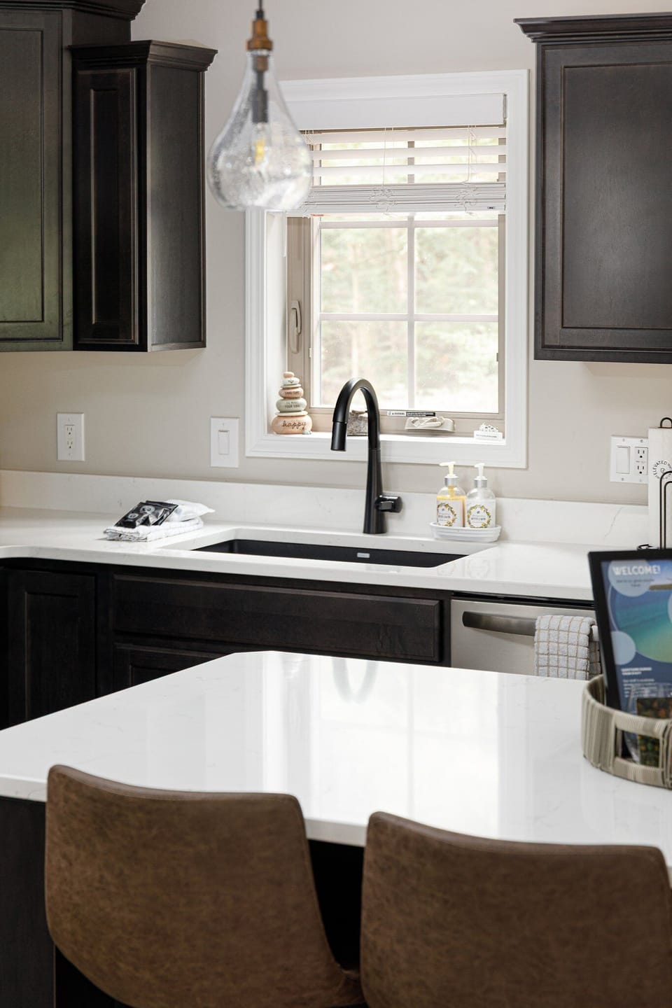 Sunlit kitchen sink area w/ window views & clean, modern counters.