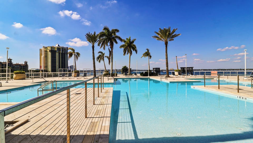 Sunny outdoor pool, relaxing deck, and tropical palm trees by the skyline.