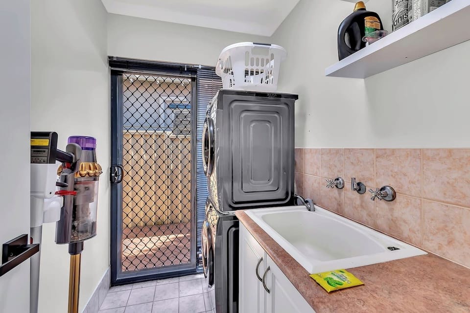 Travel light with a dedicated laundry featuring a washer, dryer, and utility sink, all tucked into a bright, practical room with direct outdoor access. A Dyson vacuum is also on hand to help keep things tidy throughout your stay.