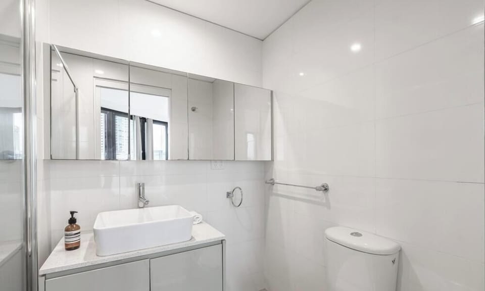 A pristine, minimalist bathroom featuring a sleek square basin, a glossy grey vanity unit, and a large mirror cabinet