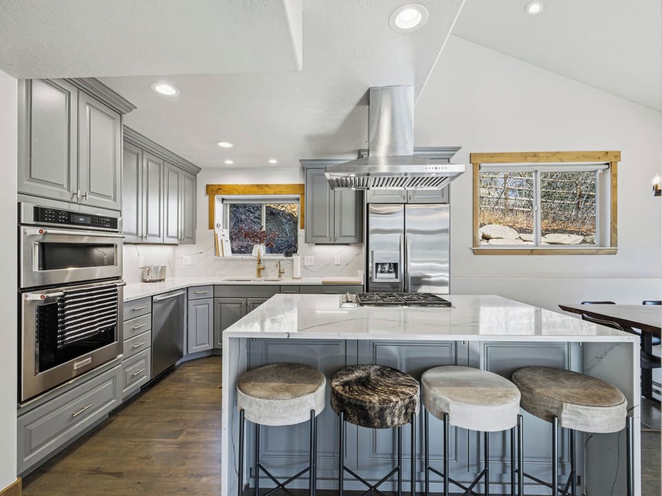 Modern chef's kitchen featuring sleek grey cabinetry, stainless steel double ovens, and a massive quartz island under soaring vaulted ceilings.