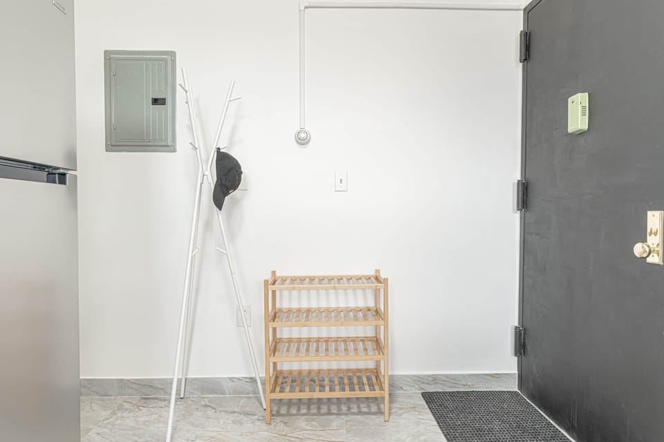 Minimal entry with a gray door, white walls, wood shoe rack, and a coat stand.