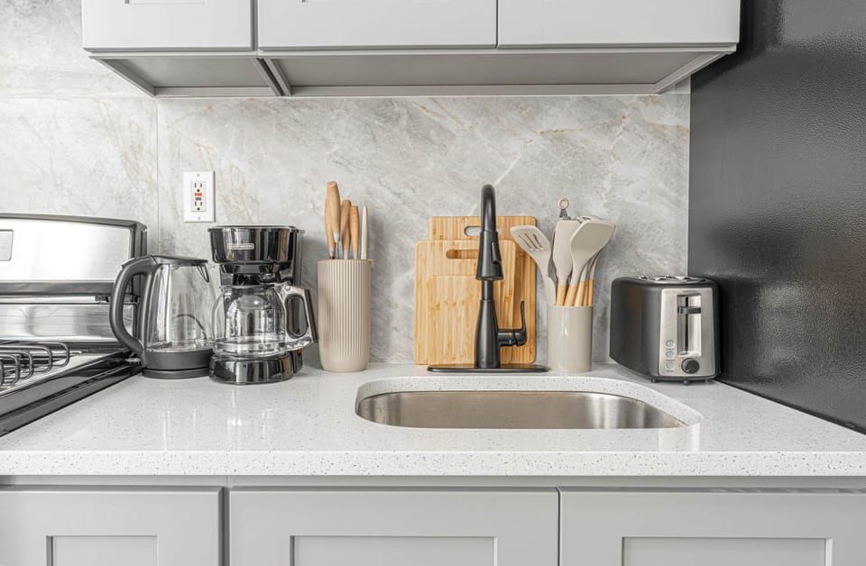 Modern kitchen counter with appliances, sink, utensils, and marble backsplash.