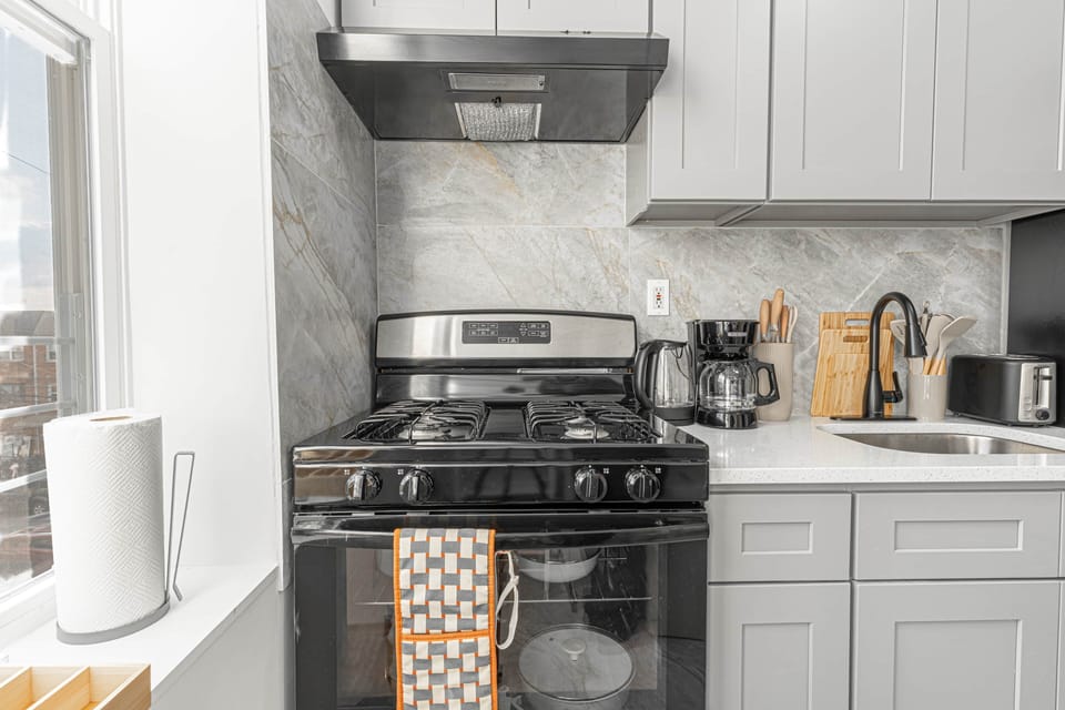 Modern kitchen with a black stove, coffee maker, kettle, sink, and white cabinets.