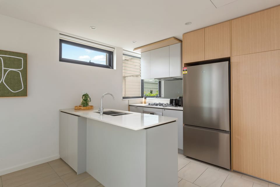 The sleek kitchen combines stone benchtops with premium appliances, including a full oven, dishwasher, microwave, and all the cooking essentials for effortless in-home dining.