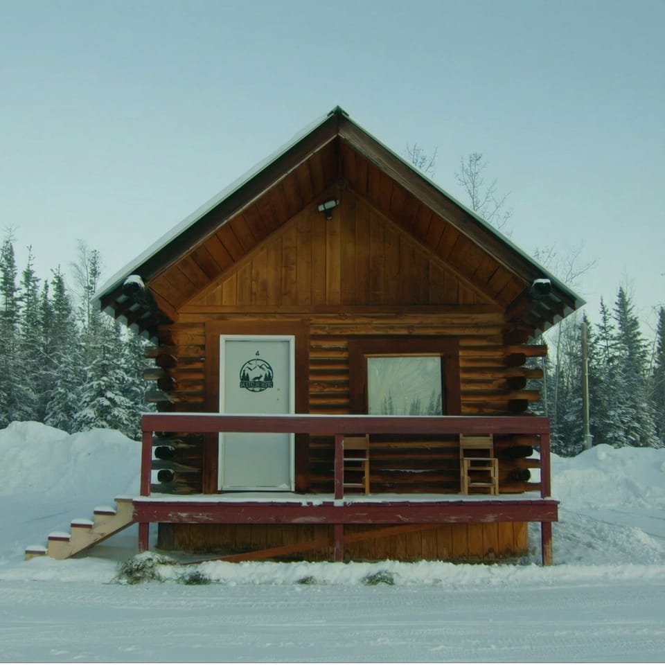 Cozy log cabin in snowy pines with porch seating—your serene winter escape.