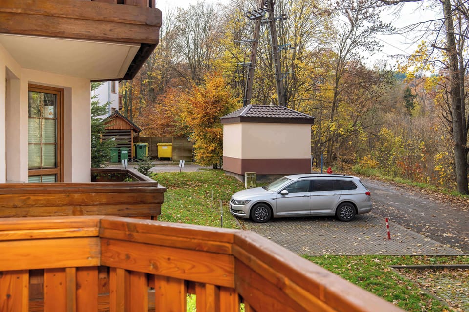A peaceful balcony view overlooking a small parking area surrounded by autumn trees. The natural scenery adds a calm and relaxing touch.