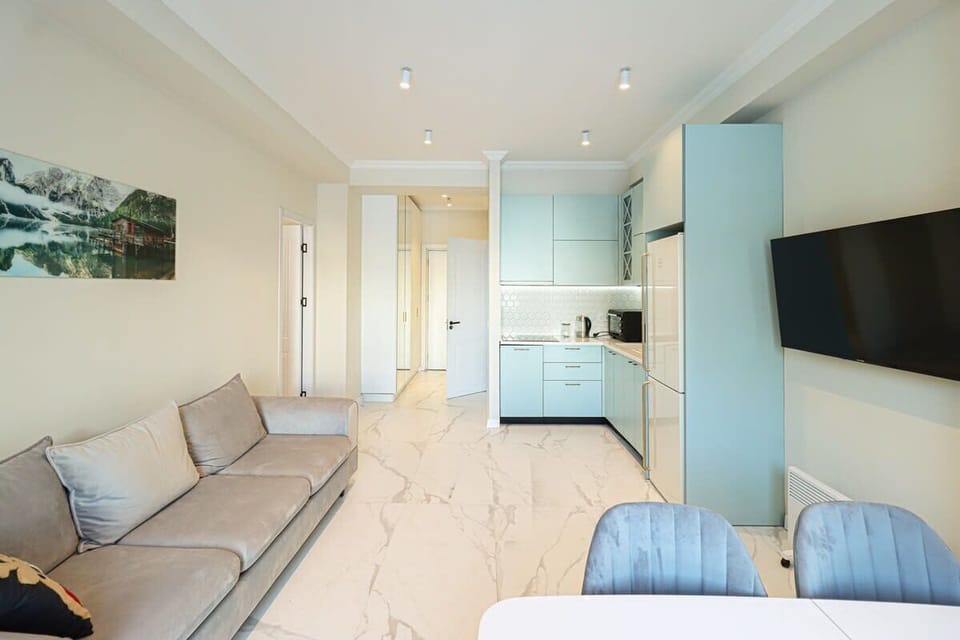 The living room features a fully equipped kitchen, a dining table, and a large sofa.