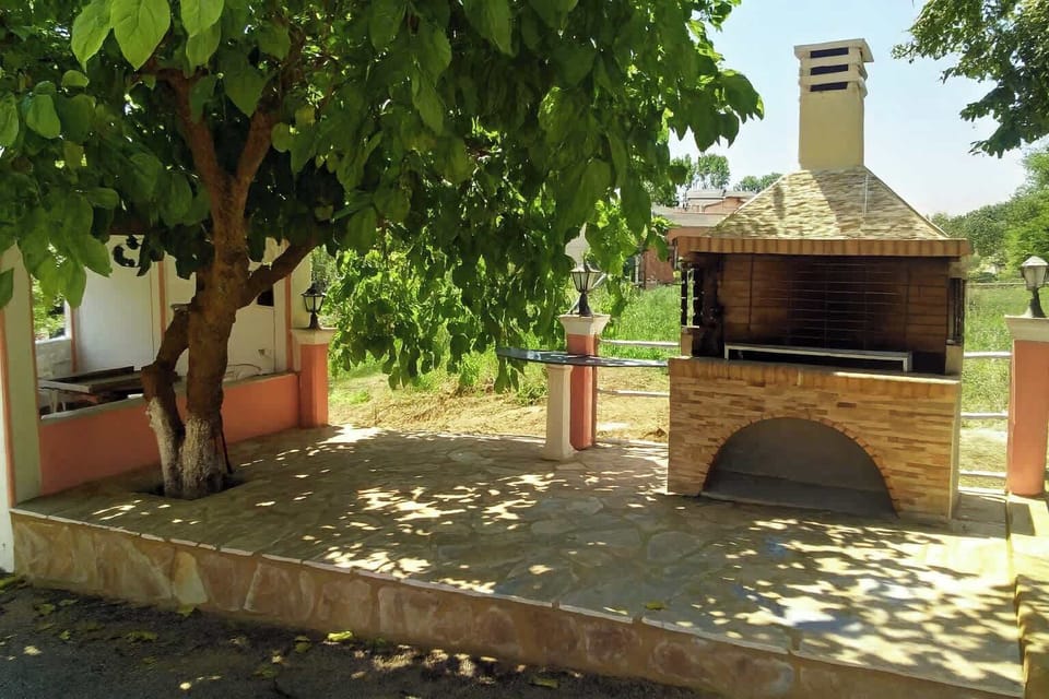 Relax in a charming outdoor space featuring a cozy BBQ area, shaded by a lush tree. Perfect for outdoor dining and enjoying peaceful moments in nature.