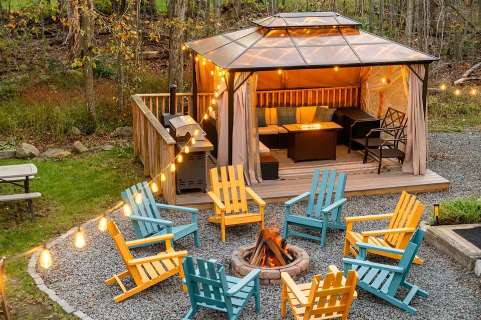 Backyard view with gazebo, grill, firepit, colorful chairs, and relaxing light.