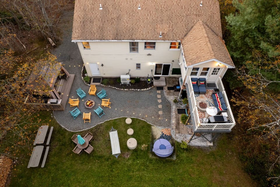 Drone view showing lawn, firepit, gazebo, and the home’s wooded surroundings.