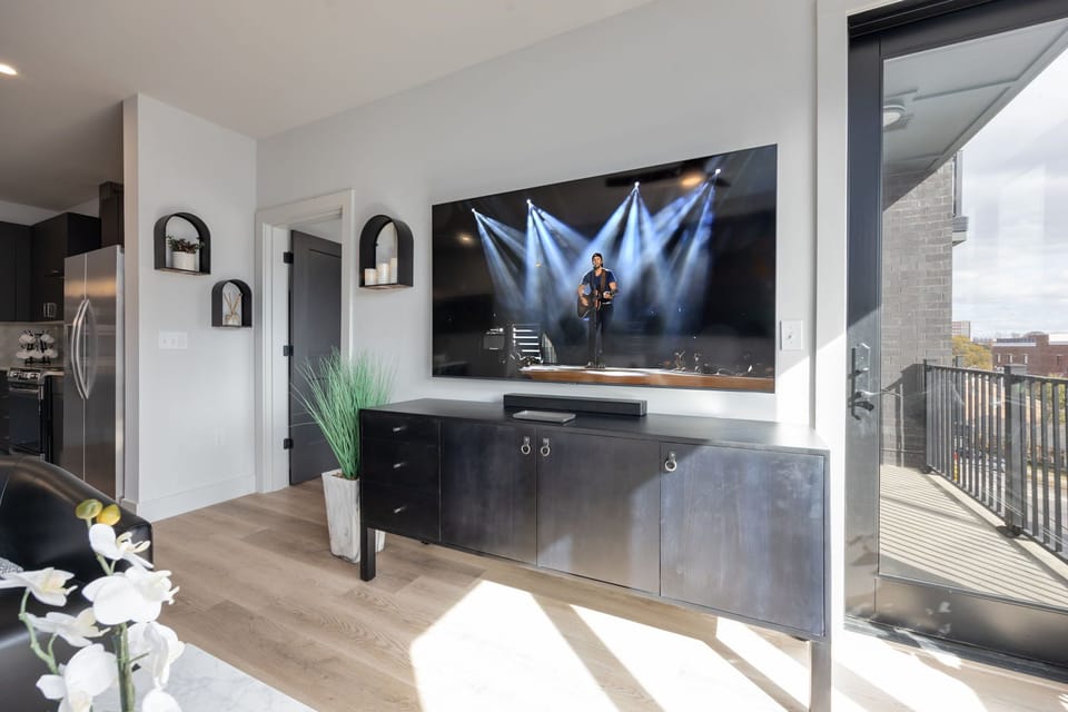 Unit 1: Modern open concept living area with floor to ceiling windows, designer furniture, smart TV, and access to private patio.