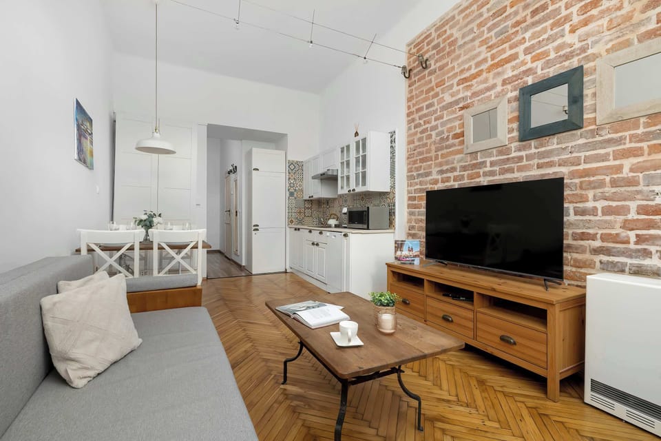 A compact living space with a grey sofa and a TV, complemented by light walls and wooden flooring. The layout maximizes comfort and functionality.