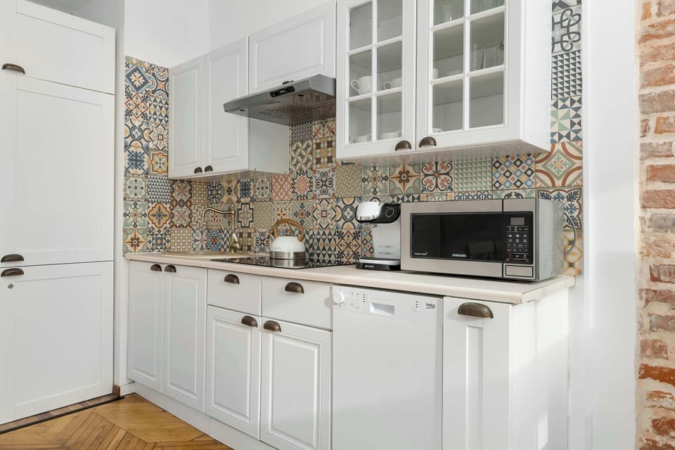 A bright kitchen space with white cabinets, microwave, and oven, featuring a decorative backsplash and brick accents. It offers a functional and stylish cooking environment.