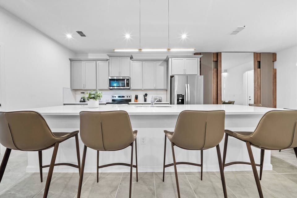 This bright and airy kitchen boasts sleek white cabinetry and modern stainless steel appliances, inviting you to unwind at the stylish island bar stools, while warm wooden accents enhance your culinary experience.