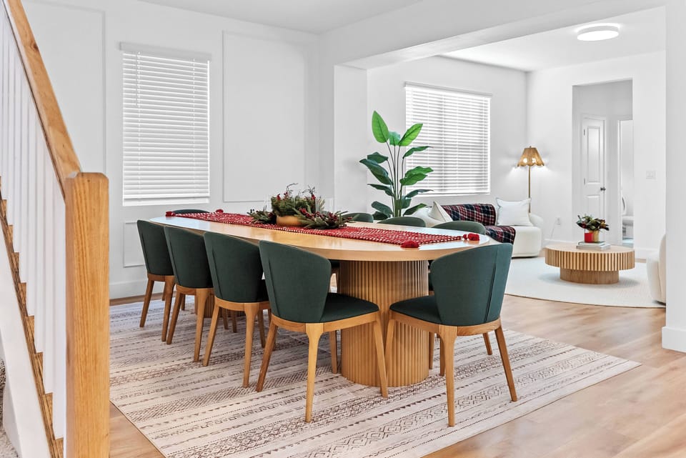 Gather at the beautiful wood dining table, surrounded by vibrant green chairs that brighten the warm tones. Sunlight fills the room, enhancing the inviting textures and lush plants for a truly welcoming atmosphere.