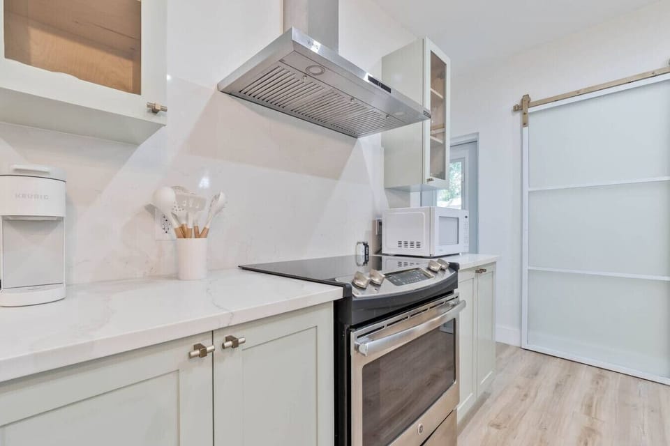 Kitchen with electric range, range hood, white cabinets and barn door