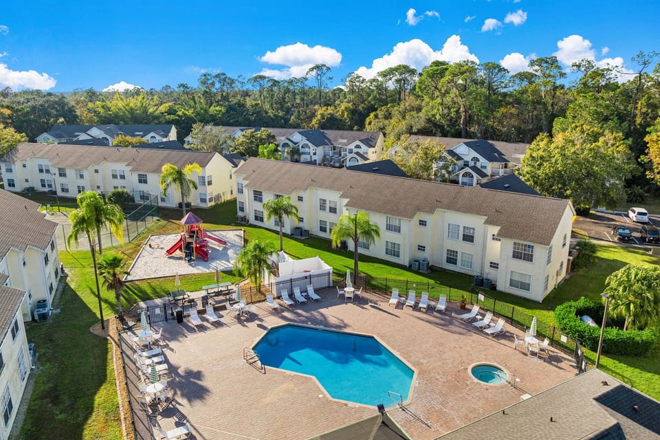 Community Aerial – Beautiful birds-eye view of the pool area, hot tub, and nearby playground for family fun.