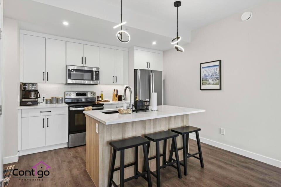 Sleek, fully stocked kitchen featuring a quartz breakfast bar, full-size stainless steel appliances, and stylish pendant lights — everything you need for a home-cooked meal during your Canadian Rockies vacation rental stay.