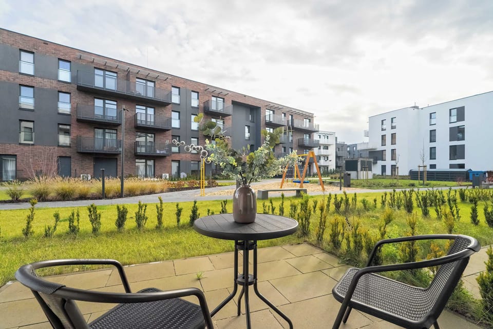 A private terrace with a small table and two chairs overlooking a green, well-kept courtyard. It offers a peaceful outdoor space ideal for morning coffee or relaxing in the fresh air.