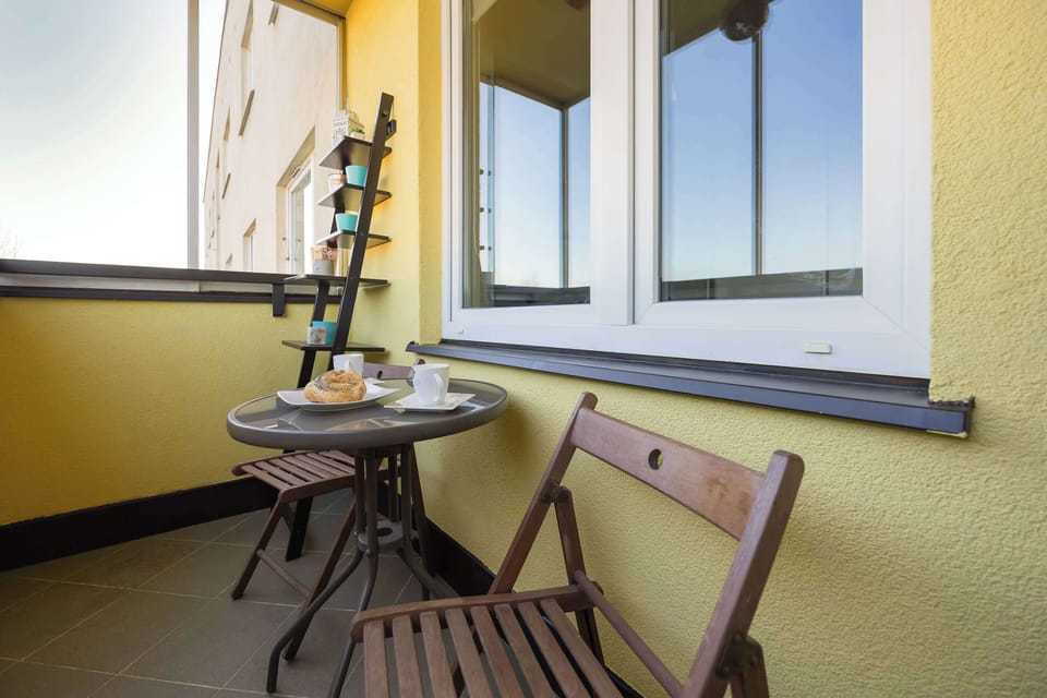 A small enclosed balcony with a table and two chairs. The yellow wall adds a cheerful touch to the relaxing corner.