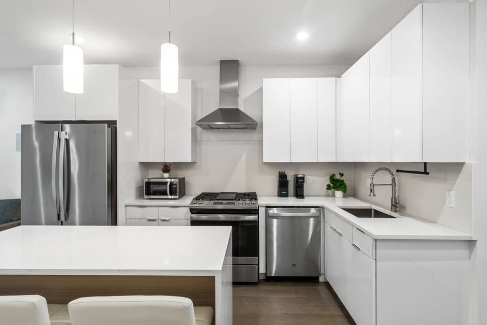 A bright, fully equipped kitchen showcasing the stainless steel fridge, gas range, microwave, dishwasher, and deep sink with a flexible pull-down faucet. Simple. Modern. Easy to use.