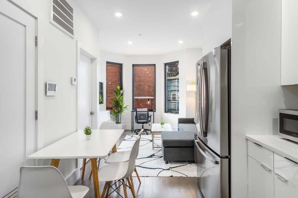 A bright open layout with a cozy sectional, a sleek dining table for four, and large windows that pull in tons of natural light. The space feels modern, clean, and easy to settle into.