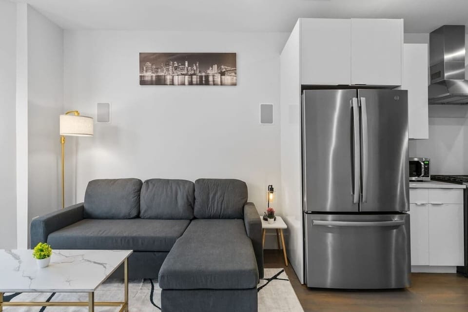This angle highlights the sectional alongside the stainless steel fridge. The layout shows how seamlessly the living room flows into the kitchen.