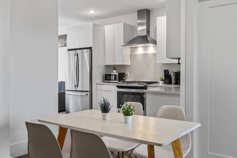 A bright dining setup with a modern white table and minimalist chairs. This angle opens directly to the sleek kitchen, keeping meals and conversation flowing naturally.
